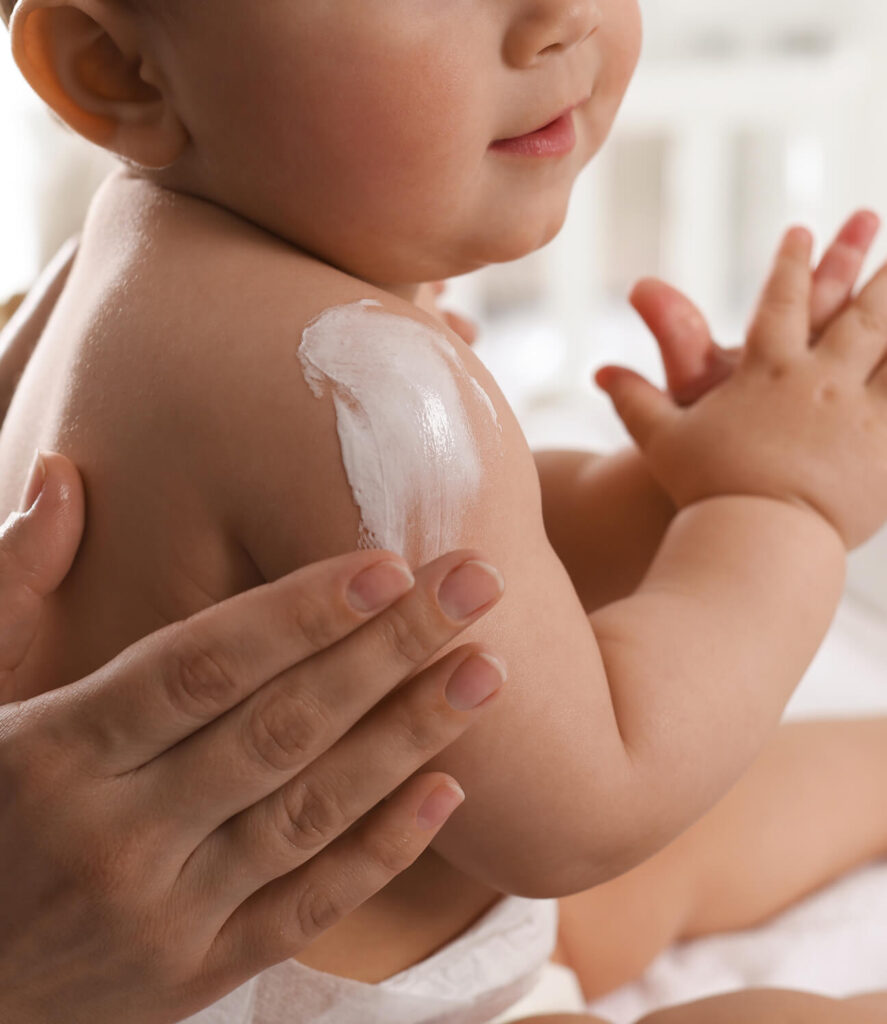 Mutter trägt sanfte Feuchtigkeitscreme auf den Arm ihres lächelnden Babys für zarte Hautpflege auf.