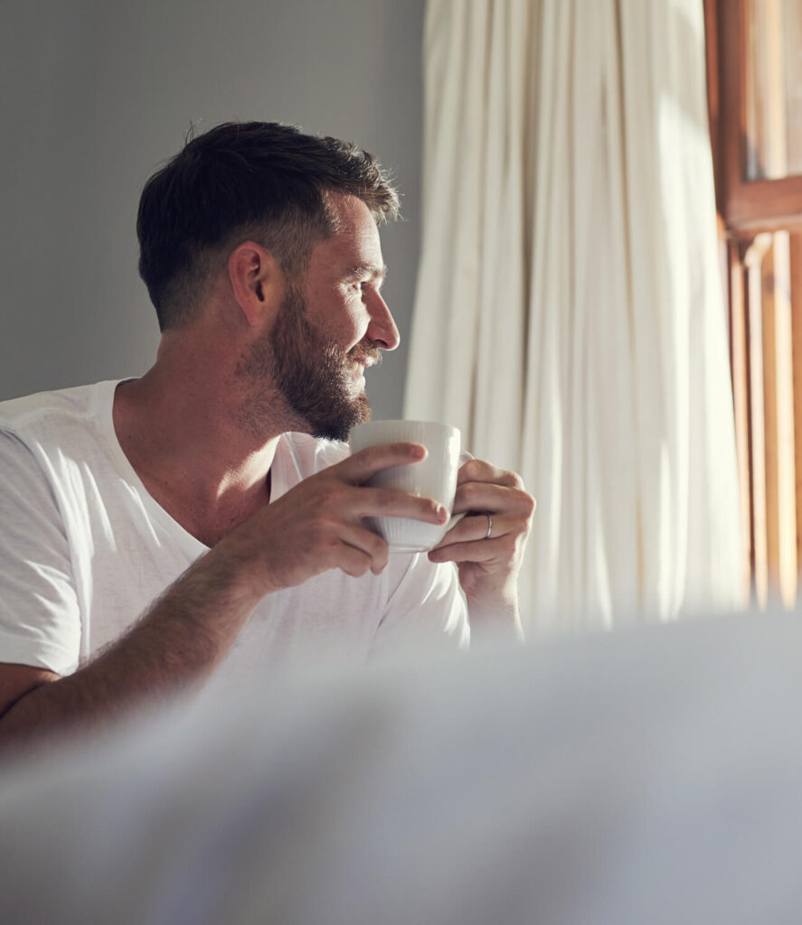 Entspannter Mann genießt morgens Kaffee im Bett für erholsame Nächte und natürliche Gesundheit.