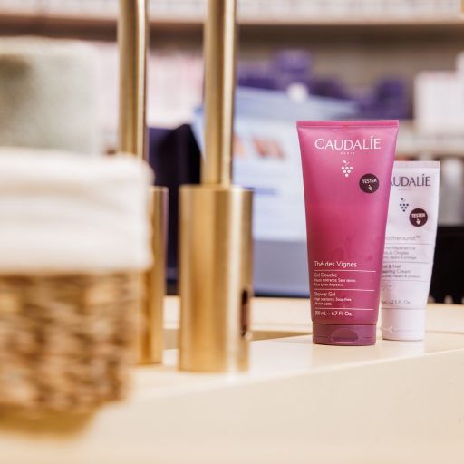 Caudalíe Pflegeprodukte in pinker Verpackung auf luxuriöser Badezimmerablage mit goldenen Armaturen und Handtuchkorb.