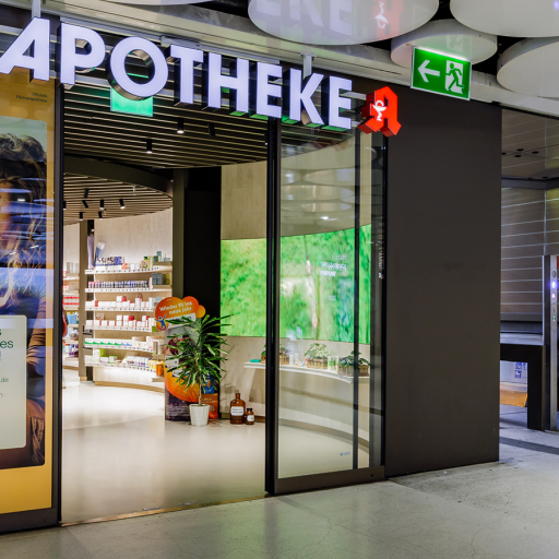 Moderne Apotheke mit grüner Leuchtreklame und Glasfront im Einkaufszentrum.